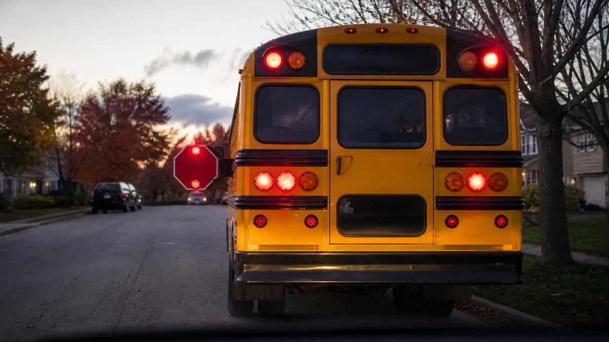 Yellow school bus stopped with stop arm extended and red lights flashing, photographed from a vehicle stopped behind it